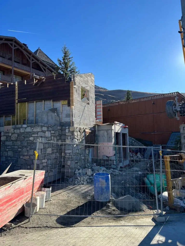Chalet exterior during renovation with stone chimney and mountain view