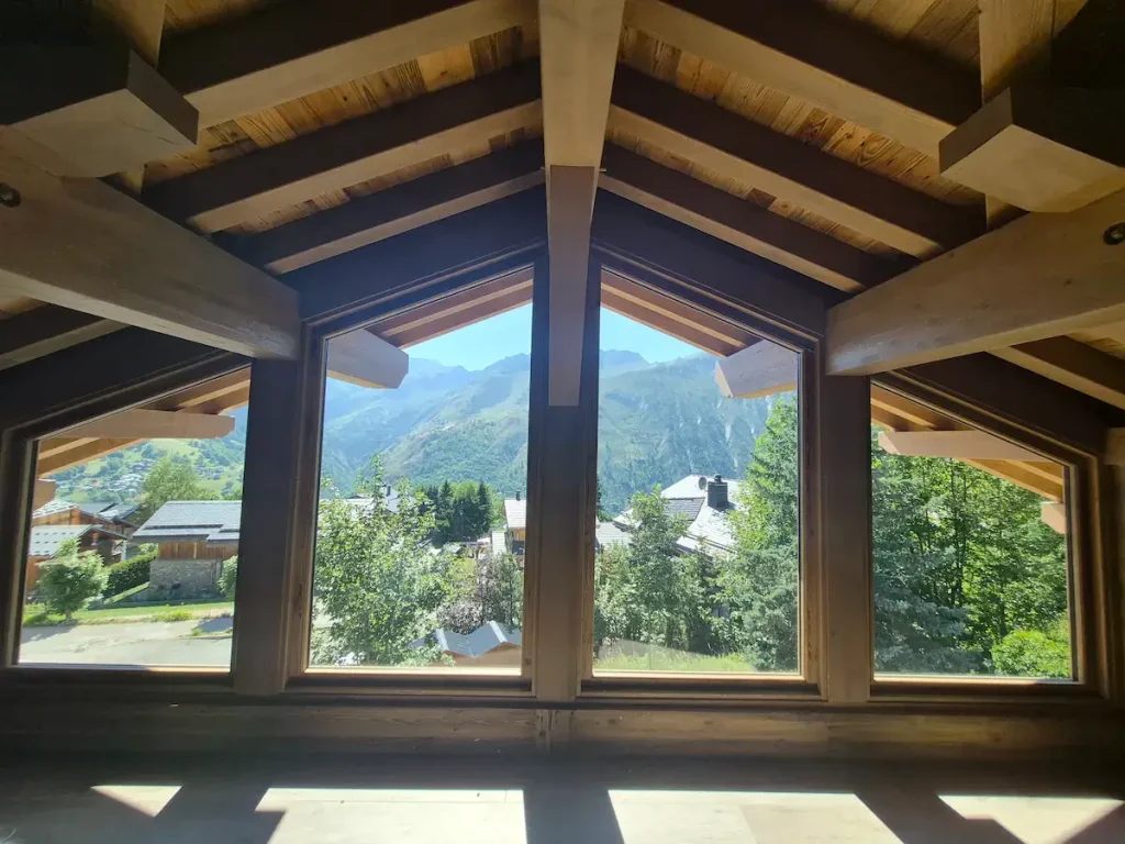 Large chalet window framed by exposed timber beams with mountain views